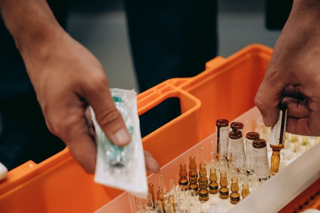 Close-up of hands organizing vials and syringe in a medical first aid kit, emphasizing emergency readiness.